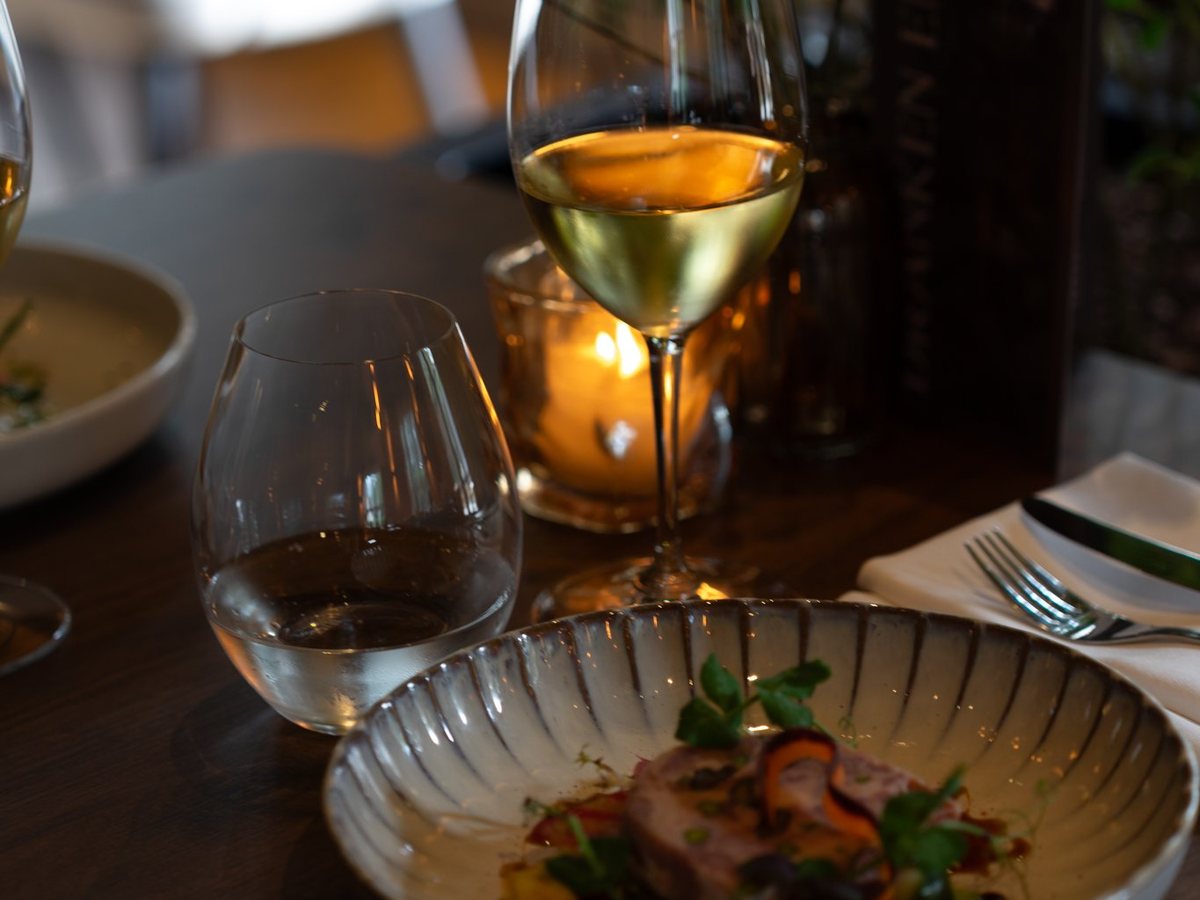 Een glas witte wijn bij kaarslicht naast een bord op tafel