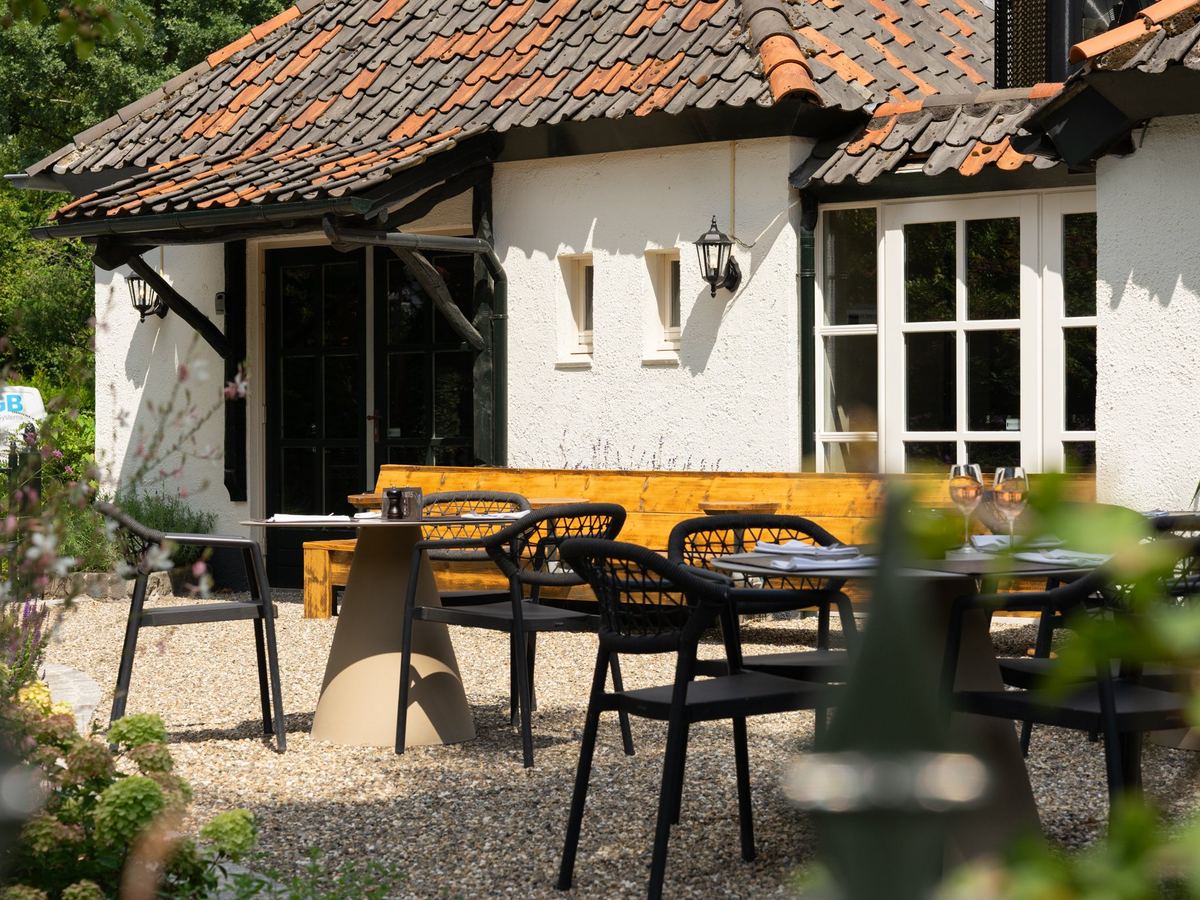 Het terras van Brasserie Bij Floor met houten tafels en zwarte stoelen voor het pand